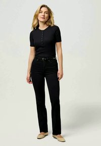 Top corto de manga corta negro con canalé y tapeta de botones, combinado con jeans negros de pierna recta. La modelo lleva unas bailarinas beiges. Diseño sencillo, silueta ajustada.
