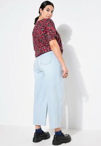 Blommig svart och röd kortärmad topp i kombination med ljusblå vida jeans och kraftiga svarta skor; har subtila texturer och fickdetaljer.