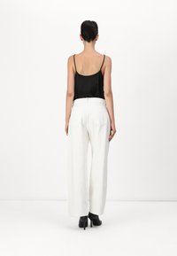 Camisola in satin nero con spalline sottili, abbinata a pantaloni bianchi a gamba larga con vita alta e scarpe nere con tacco. Design semplice e moderno.