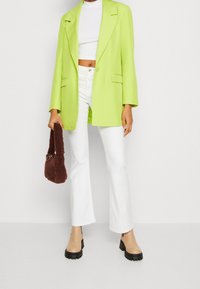 Zielony neonowy blezer z klapami z wcięciami, zestawiony z białym krótkim topem i białymi dzwonowatymi dżinsami. Brązowa futrzana torba i beżowe botki na platformie.