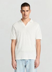 Polo blanc à manches courtes avec motif en losanges texturé, col ouvert et coupe ajustée. Associé à un jean en denim bleu clair.