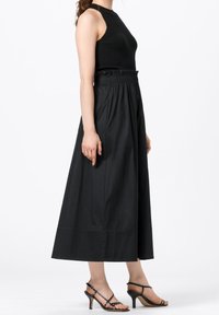Svart ärmlös topp kombinerad med en svart, ankellång kjol med elastisk midja och slät yta, kompletterad med remsandaler.