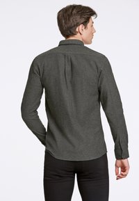 Camisa de manga larga verde oscuro con cuello abotonado, corte slim fit, tejido texturizado y dobladillo recto. Presenta un pliegue en la parte posterior y puños abotonados.