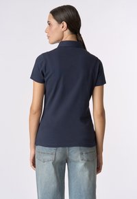 Polo blu navy con colletto classico, maniche corte e vestibilità su misura, abbinato a jeans in denim azzurro con tasche posteriori.