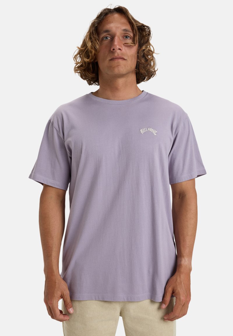 Camiseta de algodón de color púrpura claro con mangas cortas y cuello redondo, que presenta un pequeño logo blanco en la zona del pecho izquierdo.