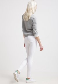 Sudadera de algodón gris con puños blancos, combinada con jeans blancos ajustados y zapatillas blancas con detalles en verde. Vista trasera.
