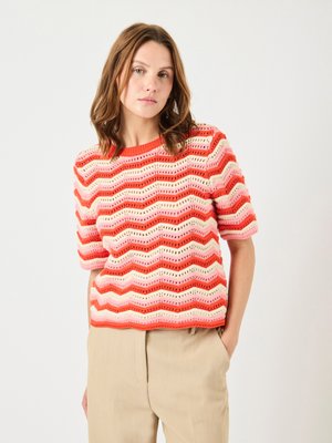 Rood en roze gestreepte gebreide trui met een golfpatroon, korte mouwen en een ronde halslijn, gecombineerd met beige broeken.