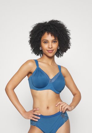 Soutien-gorge à armatures bleu marine en tissu lisse avec un mesh transparent en haut, doté de bretelles réglables et d'un petit fermoir central. Culotte bleue assortie avec des accents en dentelle.