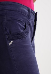 Navyblauwe stoffen broek met een textuurontwerp op de zak, featuring een decoratieve zilveren accent. Slim fit met een gladde afwerking.