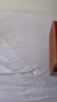 Caixa retangular vermelha e amarela com superfície texturizada e padrões impressos, colocada sobre um fundo de tecido branco amassado.
