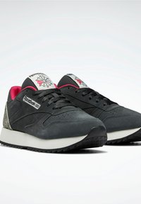 Svarta mockaskor med rosa detaljer och en vit mellansula. Har en logotyp på tungan och texturerad häldekoration. Platt gummisula.