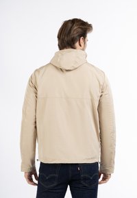 Beige lichtgewicht jack met een capuchon, met een gladde textuur en een iets losse pasvorm, gecombineerd met donkerblauwe jeans.