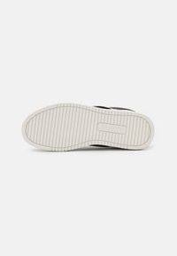 Sneaker nera con suola in gomma testurizzata, caratterizzata da scanalature orizzontali e una suola intermedia bianca. Il marchio è stampato a caldo sul lato.