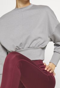 Felpa grigia a taglio corto con maniche ampie, raccolta in vita. Abbinata a leggings bordeaux a vita alta con una texture liscia e cuciture.