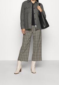 Giacca button-up in misto lana grigia, top nero, pantaloni a gamba larga in plaid verde e beige, e stivaletti beige con tacco e finitura testurizzata.