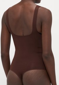 Brown bodysuit made of smooth, stretchable fabric featuring wide straps and a low back design, emphasizing a fitted silhouette.