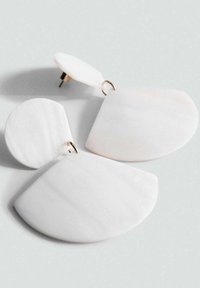 Witte geometrische oorbellen van glad materiaal, met een cirkel- en een halve maanvorm, voorzien van accenten in goudkleurige hardware.