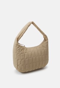 Quiltet beige taske med blød tekstur, buet silhuet og en enkelt skulderrem. Har en lynlåslukning og horisontal syning.