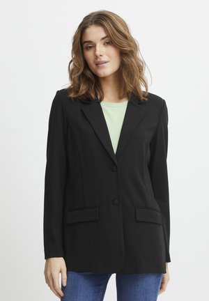 Černý blazer s klopami, dvěma předními kapsami, zapínáním na jeden knoflík a strukturovaným střihem, nošený přes světle zelený top.