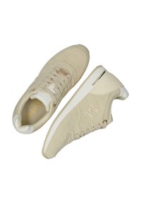 Beige stickade sneakers med en texturerad design, vit sula och guldaccent på tungan. Har rund logotyp och traditionellt snörsystem.