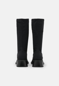 Botas negras hasta la rodilla de tejido suave, con tacón de bloque y detalles cosidos en la parte trasera, y diseño de punta redonda.