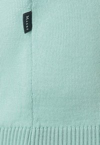 Světle mátově zelený pletený svetr s ribbeným lemem a bočním švem. Má malou černou látkovou štítku s názvem značky.