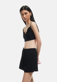 Top corto negro con tirantes finos y tela texturizada, combinado con pantalones cortos de cintura alta a juego que cuentan con una cinturilla elástica y pliegues.
