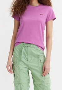 Rosa T-shirt med kort ärm och rund halsringning samt liten röd Levi's-logga, som är ihop med gröna cargobyxor med fickor och justerbart bälte.