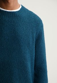 Teal textuurtrui met een geribbeld ontwerp, voorzien van een ronde halslijn en gebreide stof. De mouwen zijn iets losjes passend.