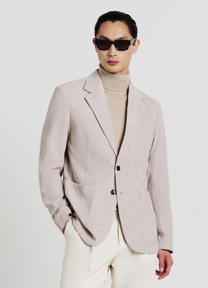 Beiger Cordblazer mit zwei Vordertaschen, Ein-Knopf-Verschluss, Revers mit Kerbung und strukturierter Stoff. Über einem beigen Rollkragenpullover getragen.