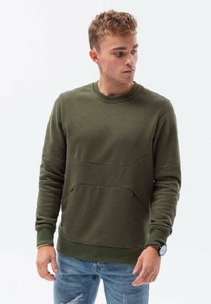 Groene sweatshirt met een textuurpaneelontwerp, ronde halslijn en contrasterende boorden. Gecombineerd met lichtblauwe jeans en een horloge.