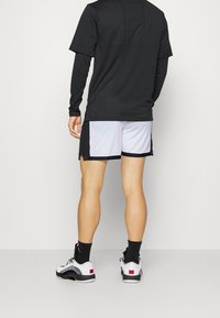 Camiseta atlética negra con textura de malla en la parte trasera, combinada con shorts gris claro con ribete negro y zapatillas deportivas blancas con acentos rojos.