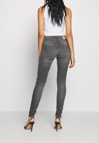 Jeans skinny grises de cintura alta hechos de denim, con bolsillos traseros y detalles desgastados, combinados con sandalias de tacón negro.
