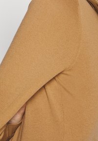 Hnědá pletená svetrka s hladkým, texturovaným povrchem. Obsahuje zaoblený manžet a viditelné švy.