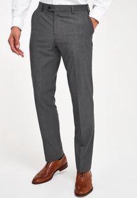 Pantalones grises ajustados con una textura sutil, que presentan un frente plano, presillas para cinturón y un cierre de un solo botón, combinados con zapatos de ala marrones.