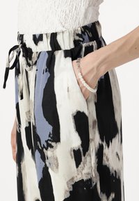 Patterned trousers with a drawstring waist, featuring black, white, and blue abstract designs. The fabric has a smooth texture and side pockets.