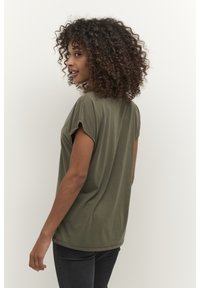 T-shirt ample de couleur vert olive en tissu doux, avec manches courtes retroussées et col rond, porté avec un jean foncé.