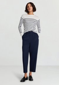 Maglione a righe in bianco e blu navy, abbinato a pantaloni blu navy con tasche e chiusura con bottone. Mocassini neri completano il look.