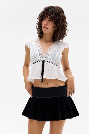 Blouse blanche à manches courtes avec des détails en dentelle et un nœud noir à la taille, associée à une mini-jupe noire évasée et froncée.