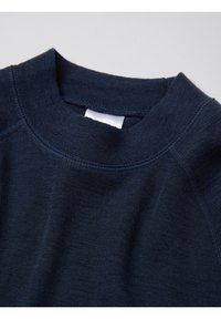 Donker marineblauw gebreide trui met zichtbare stiksels en een wit label binnenin de kraag, tegen een lichte achtergrond.