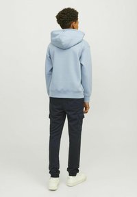 Felpa con cappuccio azzurro chiaro con polsini a coste, abbinata a pantaloni cargo blu scuro con tasche laterali e sneakers bianche.