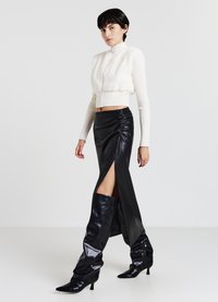 Maglione bianco corto con collo alto, abbinato a una gonna in pelle nera a vita alta con arricciature laterali e uno spacco fino alla coscia. Stivali neri alti fino al ginocchio.