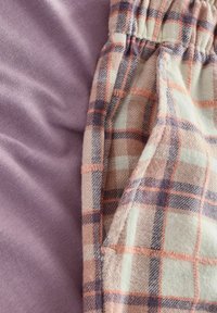 Close-up of soft purple fabric beside plaid cloth pants pocket in cream, peach, and purple tones with visible stitching and elastic waistband.