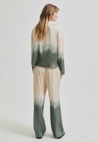 Completo in seta composto da una camicia a maniche lunghe e pantaloni a gamba larga, con una sfumatura che va dal beige al verde. Texture morbida, vestibilità comoda.