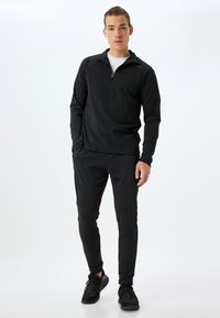 Sort atletisk top med halvlukning, parret med sorte tapered bukser. Smoother tekstur, minimalistisk design. Match med sorte sportsko.