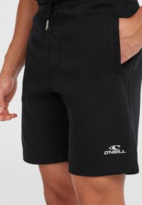 Black swim shorts made of lightweight fabric, featuring a drawstring waistband, side pockets, and a white brand logo on the lower leg.