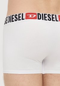 Baltas kokvilnas bokseršorti ar melnu un sarkanu "Diesel" logotipa gumiju viduklī. Gluda tekstūra, pieguļošs dizains un vidēja auguma garums līdz augšstilba vidum.