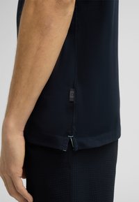 Marineblaue Performance-Hemd mit strukturiertem Stoff, seitlichem Schlitz und kontrastierenden Nähten. Verfügt über ein kleines Logo-Tag am Saum.