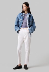 Giacca di denim, top ribbed viola, pantaloni bianchi, mocassini neri. Texture morbide, vestibilità rilassata, chiusura a bottoni, cuciture visibili e tasche a toppa.