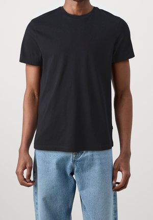 Sort bomulds T-shirt med korte ærmer, rund halsudskæring og subtilt logo-detalje. Kombineret med lyseblå jeans, der viser en afslappet pasform.